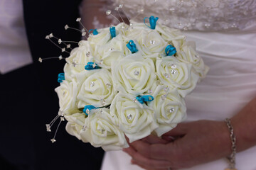 Close up of bride wearing white wedding dress, holding white rose bouquet with blue accents