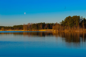 A beautiful lake in the forest, lit by the morning sun. The moon has not yet hidden