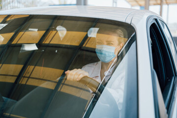  Woman with face mask driving her car during coronavirus pandemic