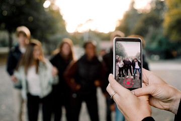 Cropped hands of woman with smart phone filming teenagers dancing on street in city