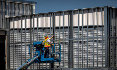 Fototapeta premium Construction worker on blue man lift working on metal prefab building