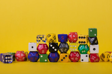 Layers of colorful game dice stacked randomly on a bright yellow background 