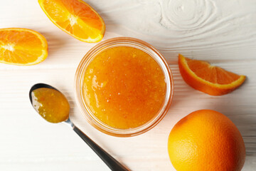 Oranges, spoon and glass jar with jam on white wooden background