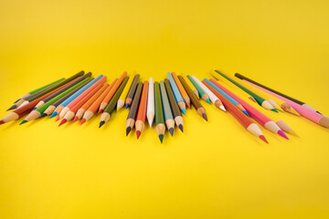 Colored pencils on a yellow background sharpened end of pencils facing camera 