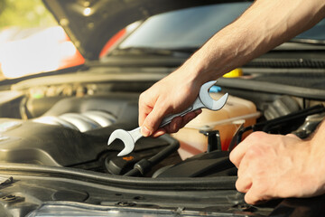 A man holds a wrench over a car engine. Car inspection