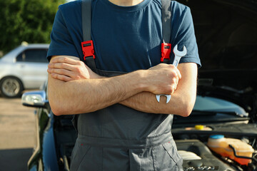 Man in overalls holding a wrench with folded arms. Car inspection