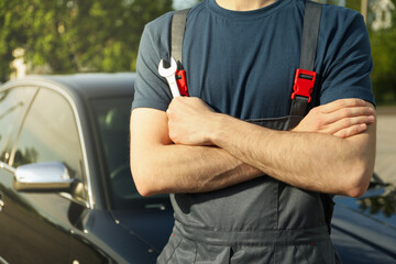 Man in overalls holding a wrench with folded arms. Car inspection