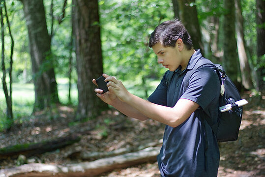 Young Man on a hike in the park taking a photo of nature with an iPhone