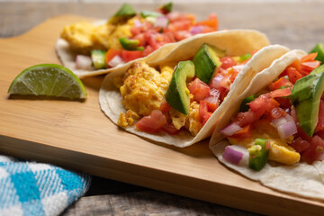 Breakfast egg tacos with flour tortilla and fresh sauce on wooden background