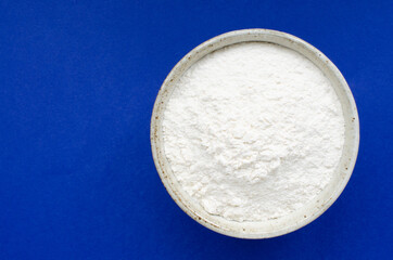 Wheat flour in bowl on blue background with copy space.