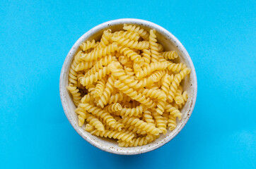 Dry noodles in bowl on light blue background. Top view.