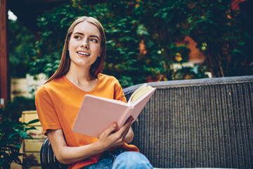Smiling thoughtful young woman with book in hands pondering on continuation of novel