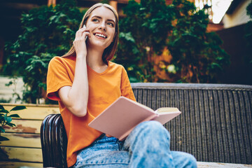 Smiling student reading diary and talking during phone conversation on smartphone device