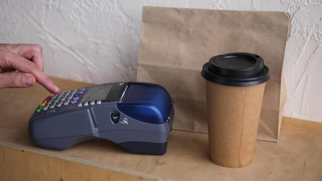 cropped view of man using payment terminal near paper bag and cup