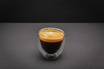 Freshly brewed creamy espresso in a glass coffee cup isolated on grey and black background, close up with copy space
