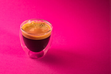 Freshly brewed creamy espresso in glass coffee cup isolated on a pink background, close up with copy space
