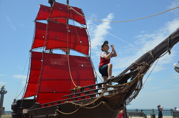 boy looks into the distance on an old ship with red sails. boy under the red sail
