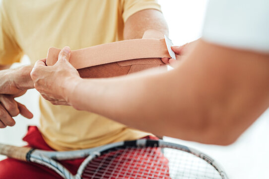 Tennis player elbow taped with elastic therapeutic or Kinesio tape applied by nurse at orthopedic ward close up image. Active sporty people health rehabilitation concept image.