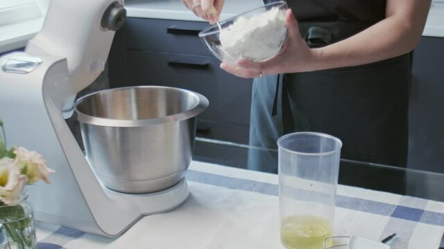 Professional chef is cooking cake. Young attractive housewife puts white cream in professional mixer