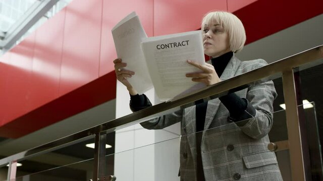 A side view slow motion video of a blonde business woman leaning on a rail and reading every page of a contract recieved from a business partner