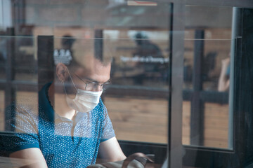 Young man works in a public cafe with protective mask