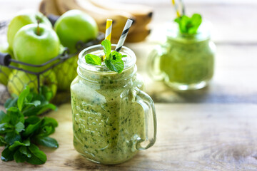 Two healthy green smoothies with spinach, banana, apple and mint in glass jar and ingredients. Detox, diet, healthy, vegetarian food concept.