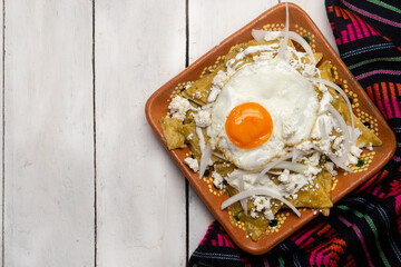 Mexican green chilaquiles with fried egg and cheese on white background