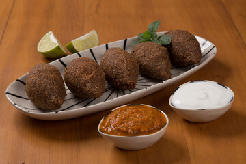 fried kibbeh served with yogurt sauce, and pepper sauce, on a plate
