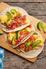 Breakfast egg tacos with flour tortilla and fresh sauce on wooden background