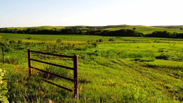 a rusty farm gate in a meadow in the green hills of Kansas in summertime