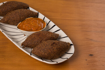 fried kibbeh served with pepper sauce, on a white plate.