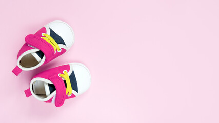Tiny sneakers for infant baby girl. Pair of baby shoes on pink background. Copy space.