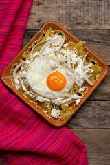 Mexican green chilaquiles with fried egg and cheese on wooden background