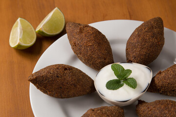 fried kibbeh yogurt sauce served on a white plate. Close up