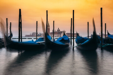 Gondolas docked at Grand Canal in Venice with Church in background. Motion blur of moving gondolas in water of canal.