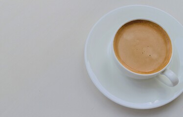 A small white cup with coffee, on a saucer on the right. Left light background for signature