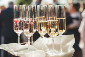 Several glasses of white wine standing on tray. Champagne with berries. Blurred guests in background. Celebration, birthday, party, wedding concept.