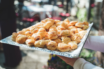 Obraz na płótnie Canvas Man holding tray with pastry. Fresh baked crispy puff pastries filled with cheese or spinach. Celebration, party, birthday or wedding concept.