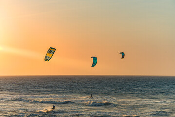 Guys flying in paragliders on the sea at sunset
