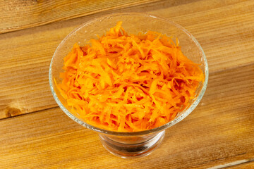 Grated carrots for salad or borsch in a glass vase on a wooden background