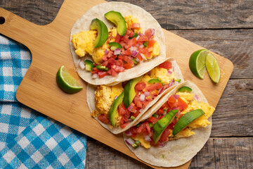 Breakfast egg tacos with flour tortilla and fresh sauce on wooden background