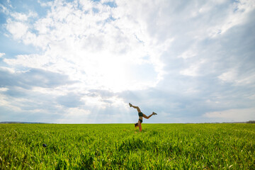 Beautiful young woman in a black top and shorts performs a handstand. A model stands on her hands, doing gymnastic splits against the blue sky. Healthy lifestyle concept