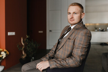 Serious man in beige checkered jaket sitting on the armchair. Groom portrait