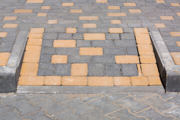 A ramp for lowering disabled people from a pedestrian sidewalk onto a pavement paved with stone...
