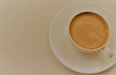 A small white cup with coffee, on a saucer on the right. Left light background for signature
