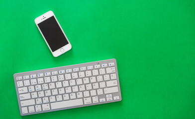 Small wireless keyboard and mobile phone, on green background, technological concept