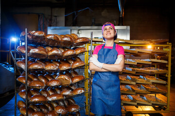 Portrait of a baker girl against the background of shelves with fresh bread in a bakery. Industrial bread production