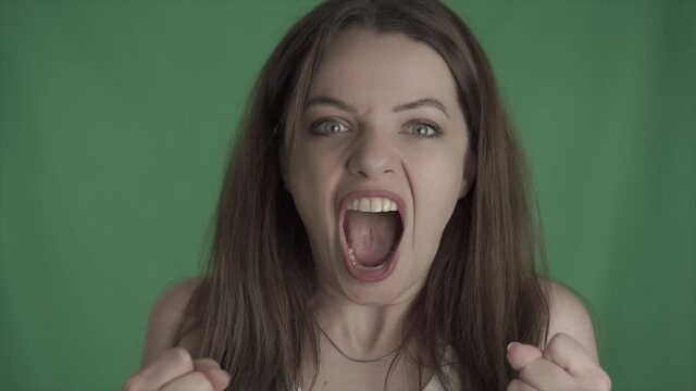 Young angry girl is screaming. Depressed, stressed beauty woman is in disappointment. Shouting female on green screen, mock up, chroma key.