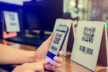 Closeup of a hand holding phone and scanning qr code. Man hand paying with qr code. Customer hand...