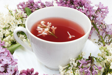 Cup of flower tea with a branch of lilac flowers on a white background, the concept of a healthy diet. Place for text, selective focus